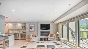 A modern kitchen with stainless steel appliances, a fireplace, and a dining area with a large window overlooking a garden. - Walk to Lifts & Village! Killington Mountain Condo (Killington)