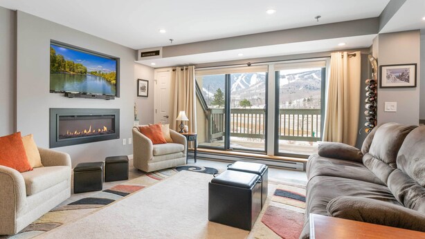 A living room with a fireplace, sofas, a coffee table, and a view of a mountain landscape through large sliding doors. - Walk to Lifts & Village! Killington Mountain Condo (Killington)