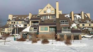 A multi-story hotel with a prominent clock on the facade, multiple balconies, and a snow-covered roof. - Walk to Lifts & Village! Killington Mountain Condo (Killington)