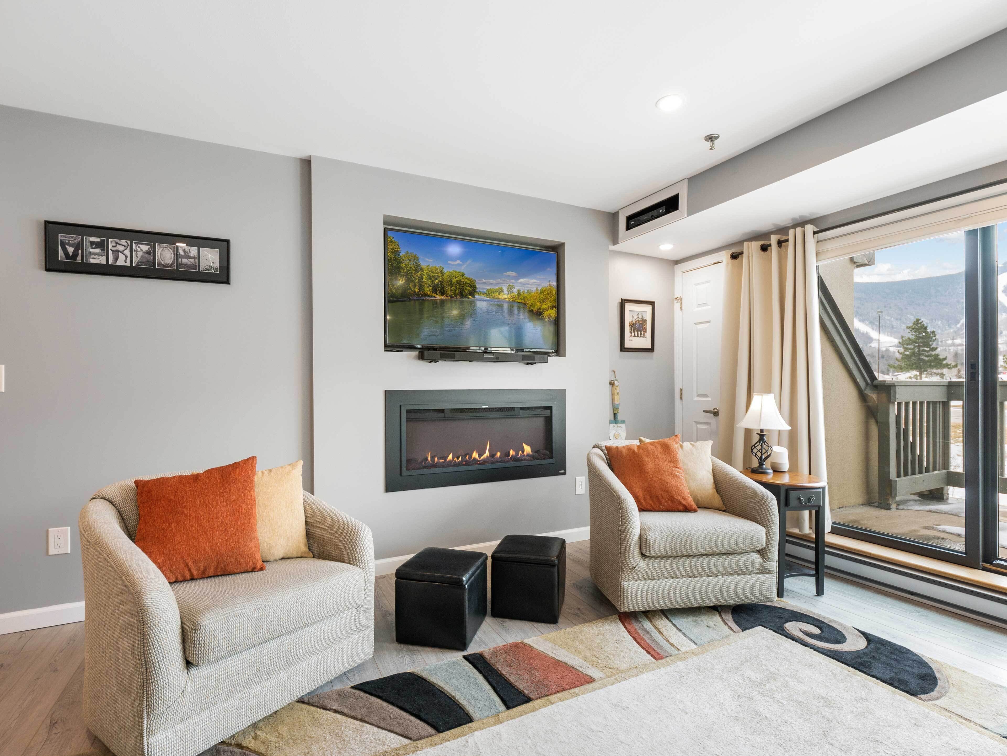 A living room with two armchairs, a fireplace, a TV, and a view of a mountain.