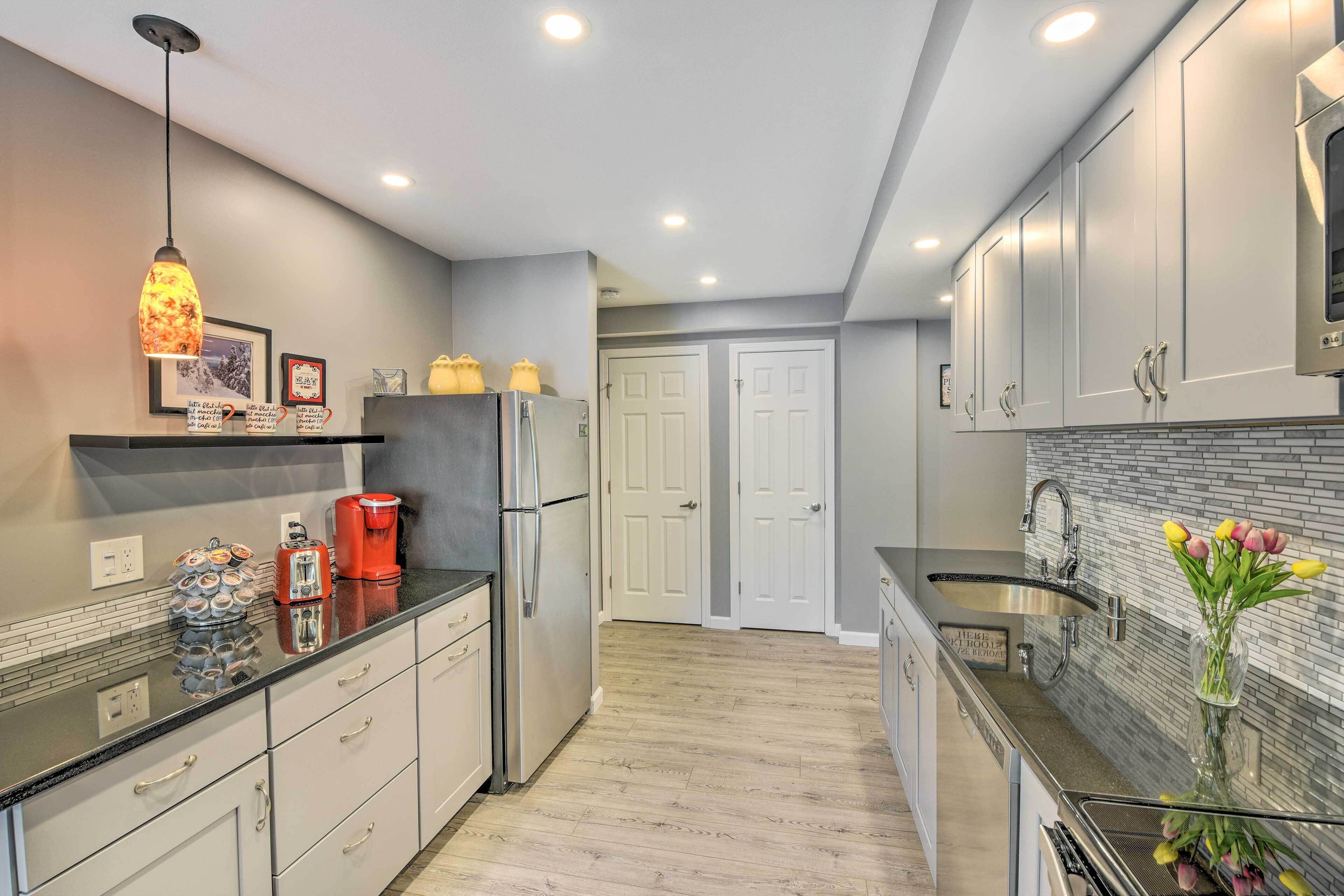 A modern kitchen with white cabinets, a black countertop, and a stainless steel refrigerator. There is a coffee maker and a vase with flowers on the counter.