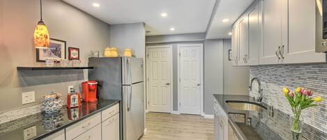 A modern kitchen with white cabinets, a black countertop, and a stainless steel refrigerator. There is a coffee maker and a vase with flowers on the counter.
