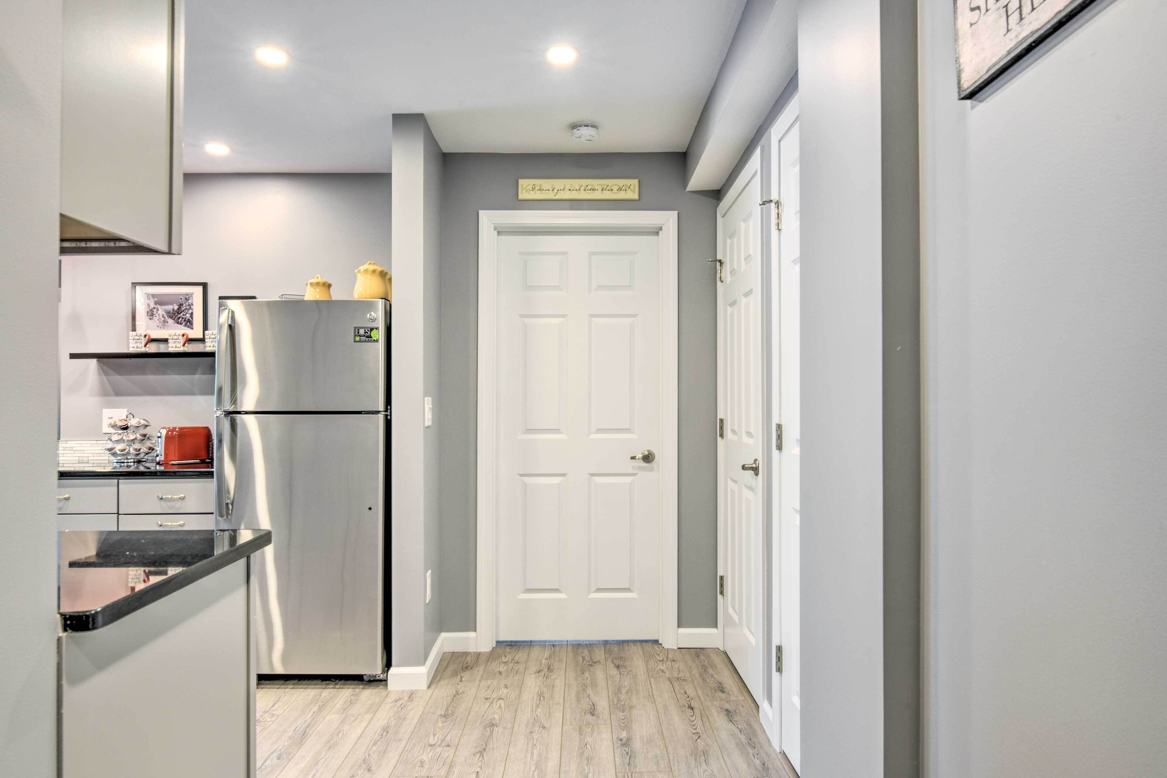 A kitchen with a stainless steel refrigerator, a wooden floor, and a white door with a sign above it.