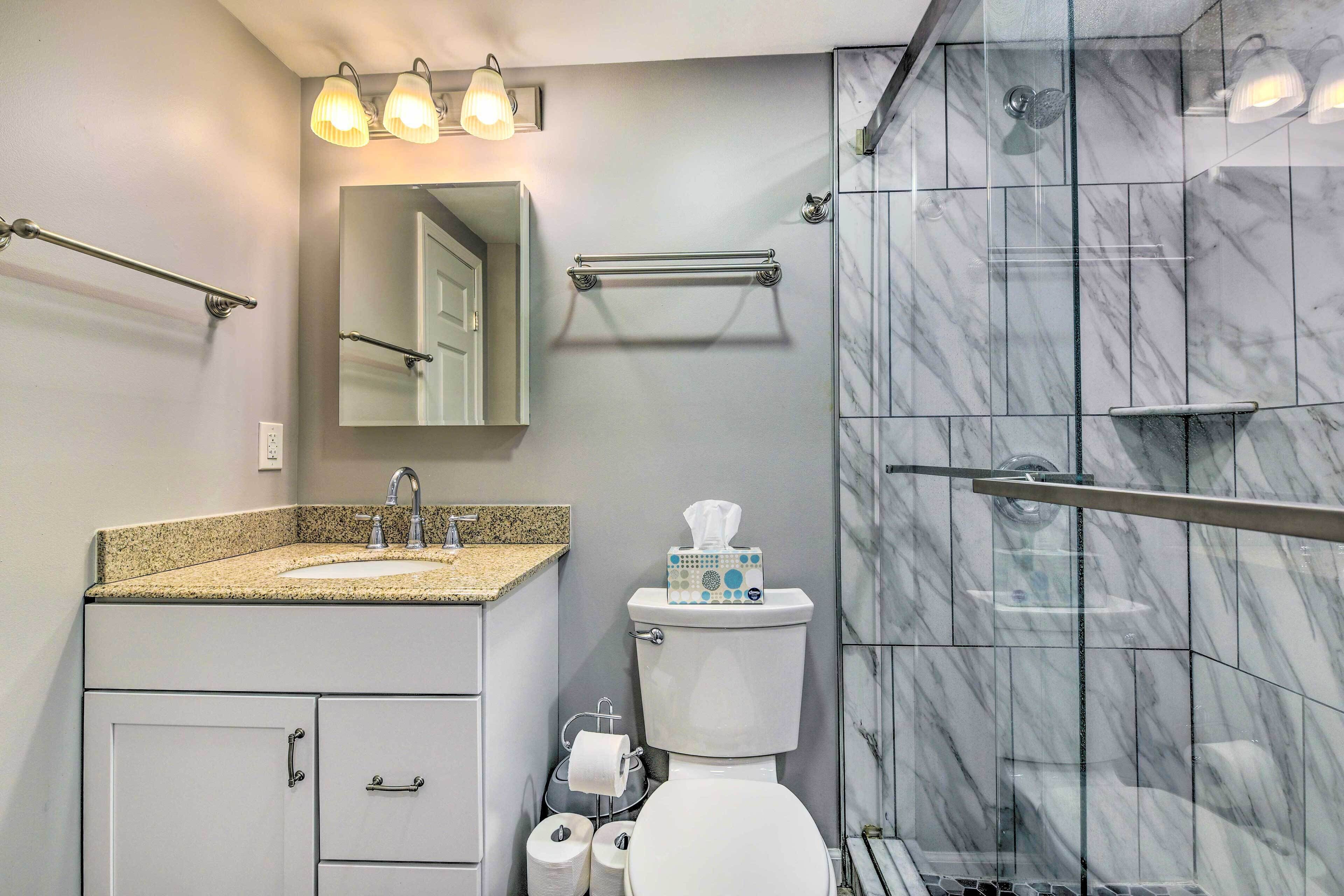 A modern bathroom with a marble shower, a sink with a granite countertop, a toilet, and a mirror above the sink.