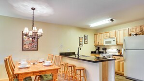 A kitchen with wooden cabinets, a central island, a dining table with chairs, and a chandelier. - Cozy Winter Park Condo w/ Hot Tub & Shuttle! (Winter Park)