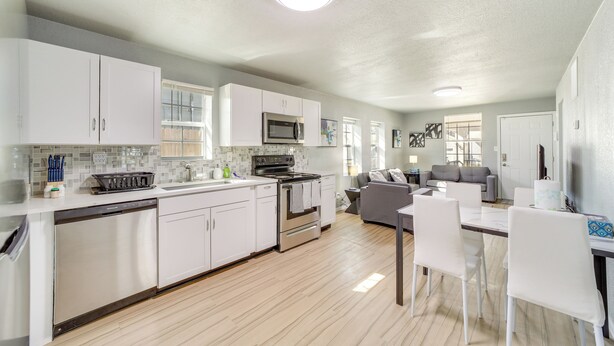 A modern kitchen with white cabinets, stainless steel appliances, and a dining area with white chairs. - Convenient Tulsa Home - 2 Mi to Downtown! (Tulsa)