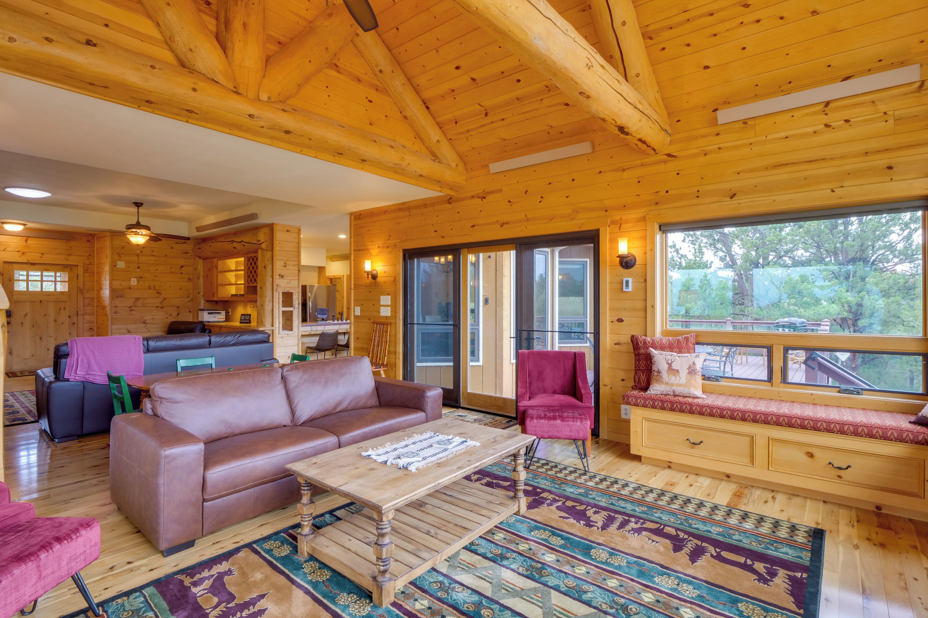 A cozy cabin interior with a wooden ceiling, a living area with a brown leather sofa, a coffee table, and a bench with cushions.