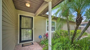 A covered porch with a door, a small garden with palm trees, and a blue sign.