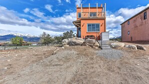 Un edificio moderno de dos pisos con balcón, ventanas amplias y vista a las montañas al fondo.