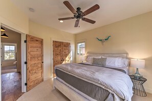 A bedroom with a large bed, a ceiling fan, wooden doors, and a small bedside table with a lamp. - Buena Vista Home w/ Mtn Views, Walk to Main St (Buena Vista)