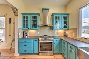 Cucina con mobili color petrolio, piano cottura in acciaio inossidabile e finestra che lascia entrare luce naturale.