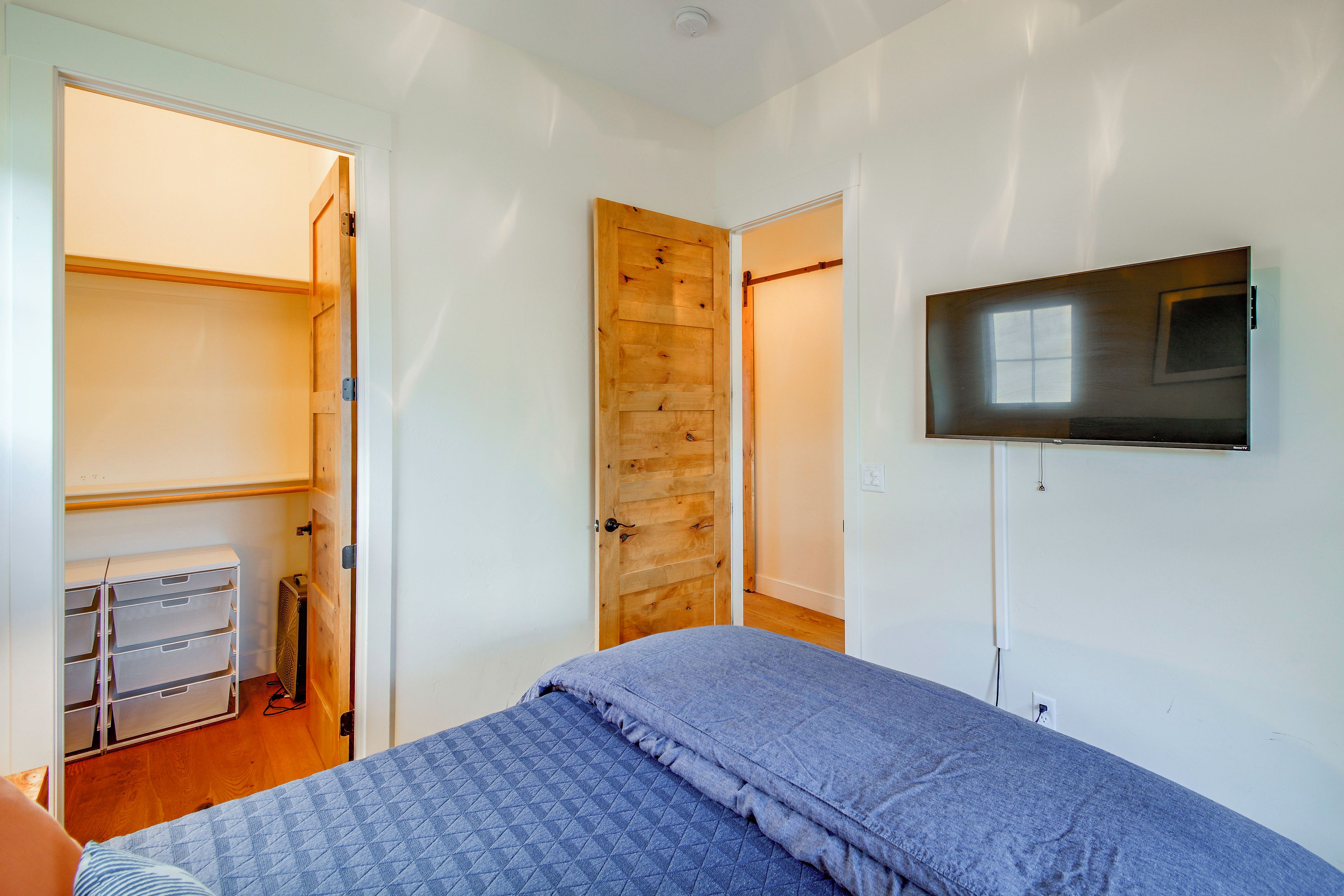 Un dormitorio con una cama, un televisor montado en la pared y un armario con las puertas abiertas.