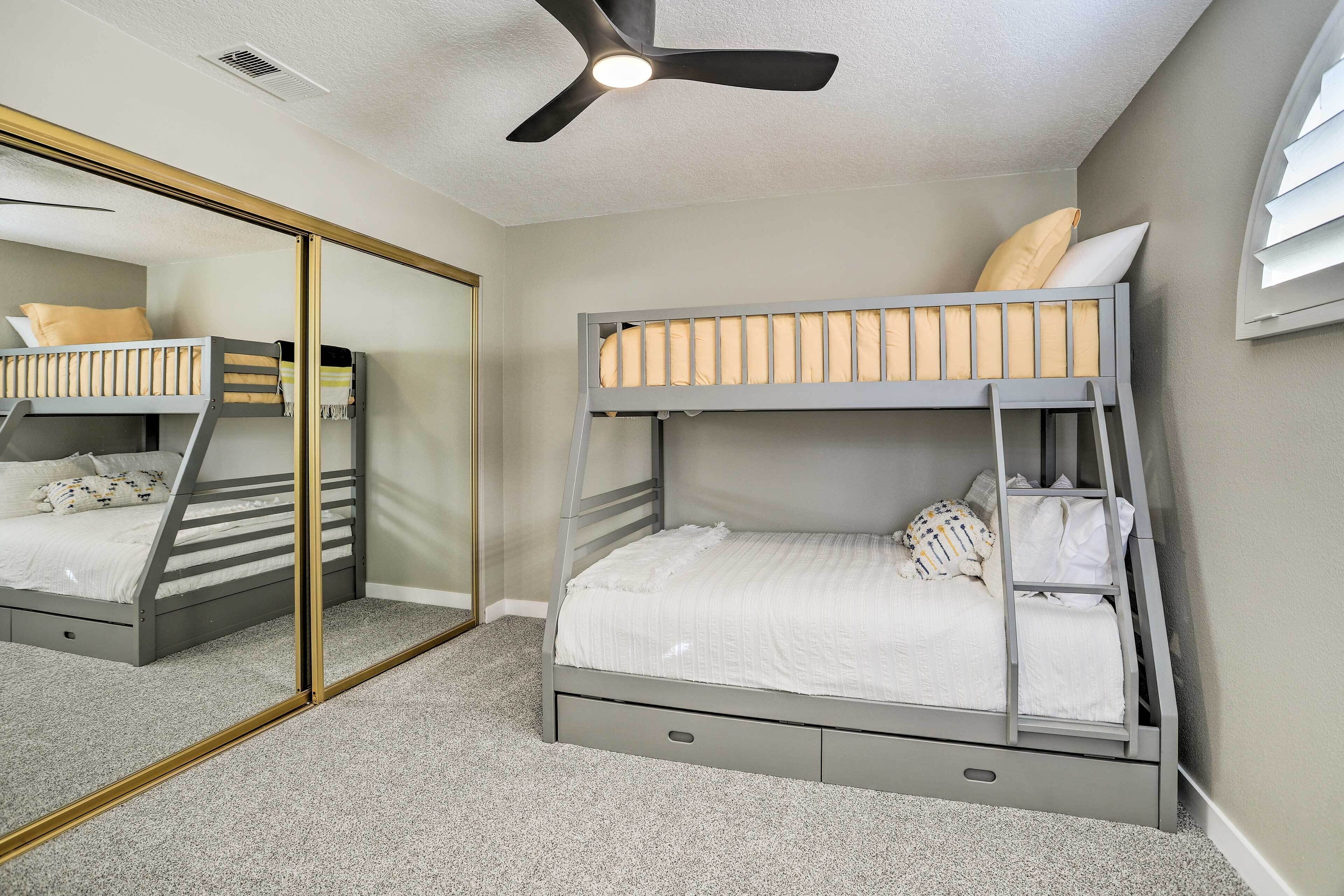 A bedroom with two bunk beds, a ceiling fan, a mirror, and a carpeted floor.