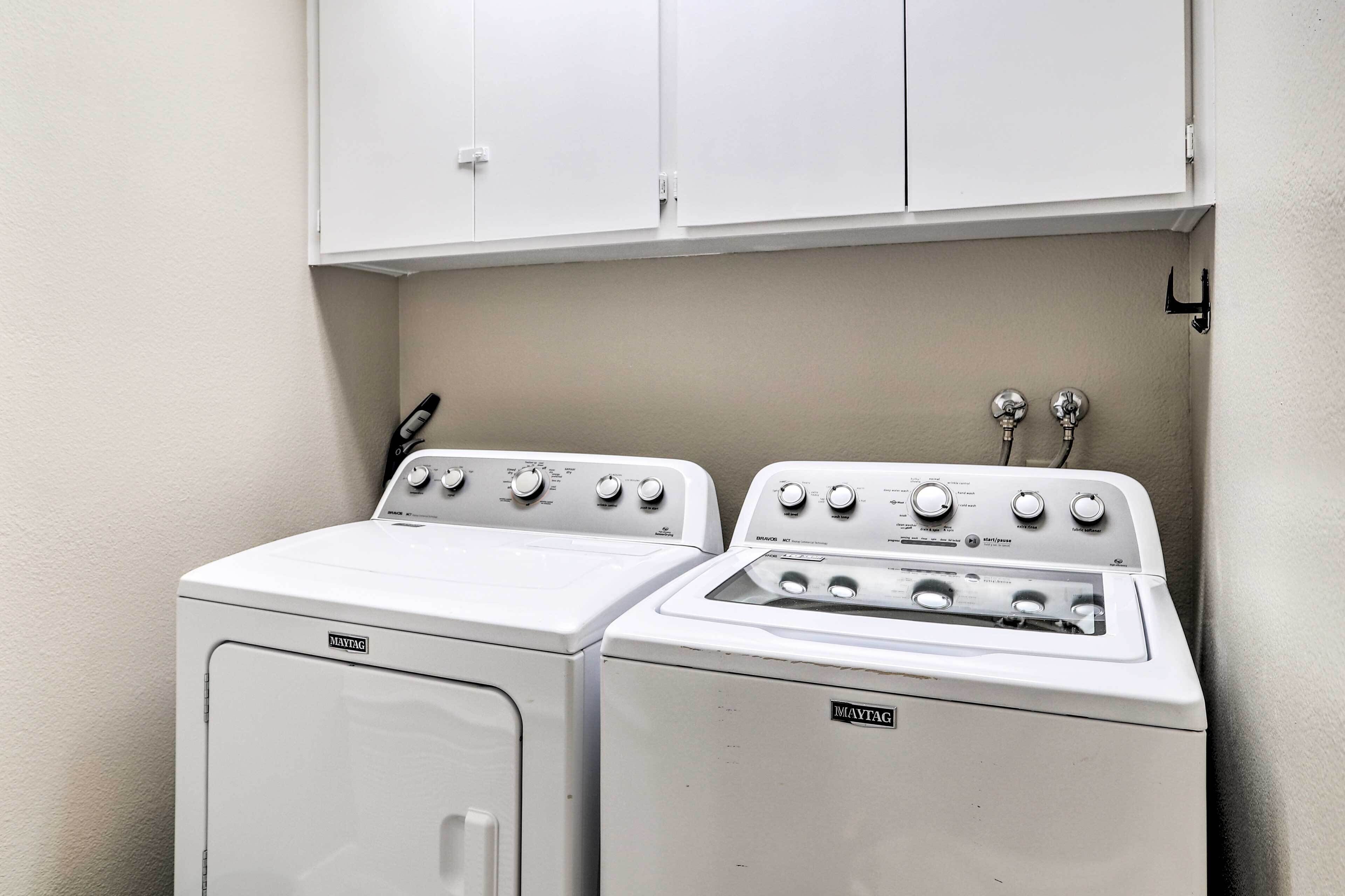 Un área de lavandería con dos lavadoras y secadoras Maytag, un gabinete blanco arriba y una lámpara fijada a la pared.