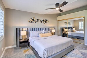 Une chambre avec un grand lit, deux tables de chevet avec des lampes, un ventilateur de plafond et un élément décoratif mural.
