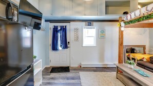 A compact living space with a kitchen area, a door with a welcome sign, a small seating area with a sofa and a coffee table, and a wooden shelf with decorative items. - 2 Mi to Dtwn & Pioneer Park: Fairbanks Studio! (Fairbanks)