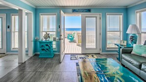 A room with a view of the beach, a teal accent wall, and a glass-top coffee table.