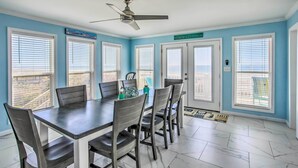 A dining area with a table and chairs, a ceiling fan, and large windows with blinds.