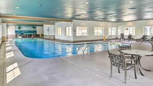 Piscina interna com água cristalina, rodeada por espreguiçadeiras e uma mesa.