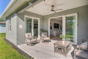 Eine überdachte Terrasse mit Gartenmöbeln, einem Deckenventilator und Glastüren, die zu einem Innenbereich führen.