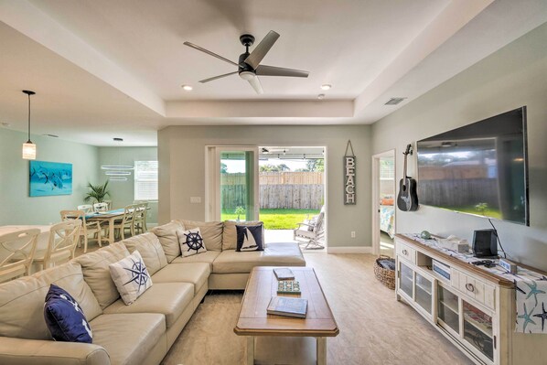 A spacious living room with a large flat-screen TV, a ceiling fan, a sectional sofa, and a dining area with a table and chairs. - 5 Mi to Beach & Walk to Park: Modern Venice Home (Venice)