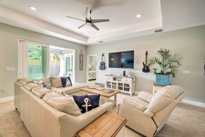 A living room with a beige sectional sofa, a wooden coffee table, a ceiling fan, a TV mounted on the wall, and a potted plant. - 5 Mi to Beach & Walk to Park: Modern Venice Home (Venice)