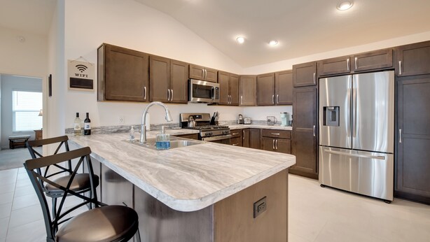 A modern kitchen with a marble countertop, stainless steel appliances, and wooden cabinets. - Sun-soaked Retreat in The Villages w/ Grill! (Coleman)