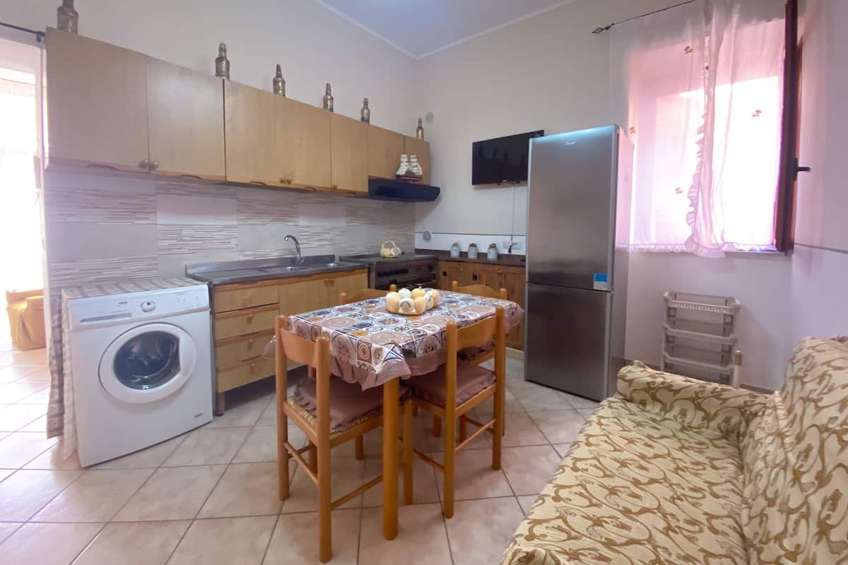 Una cocina funcional con armarios de madera, lavadora, mesa de comedor con sillas, refrigerador y ventana con cortinas.