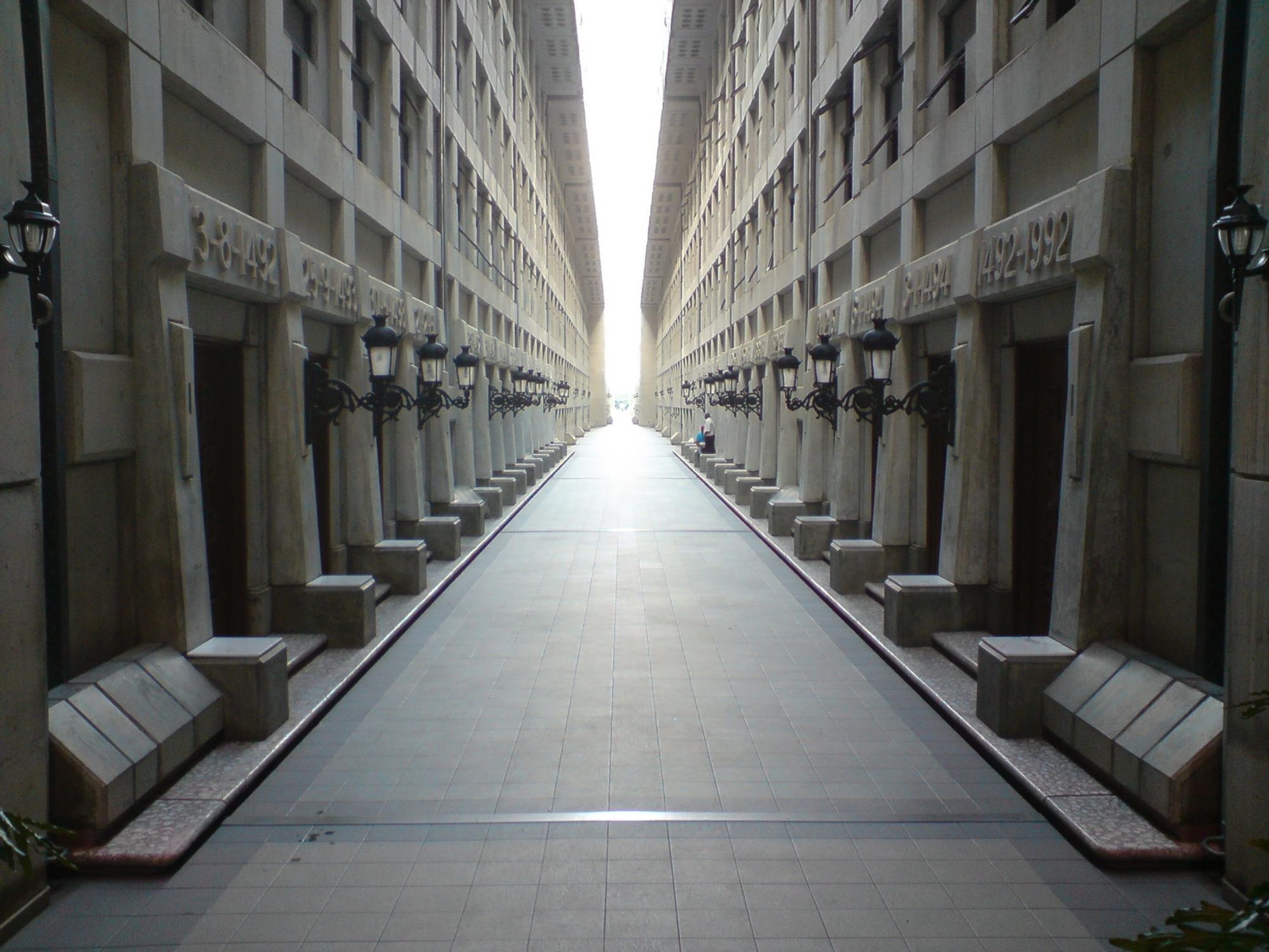 A long, straight corridor with uniform lighting fixtures and numbered doors on both sides.