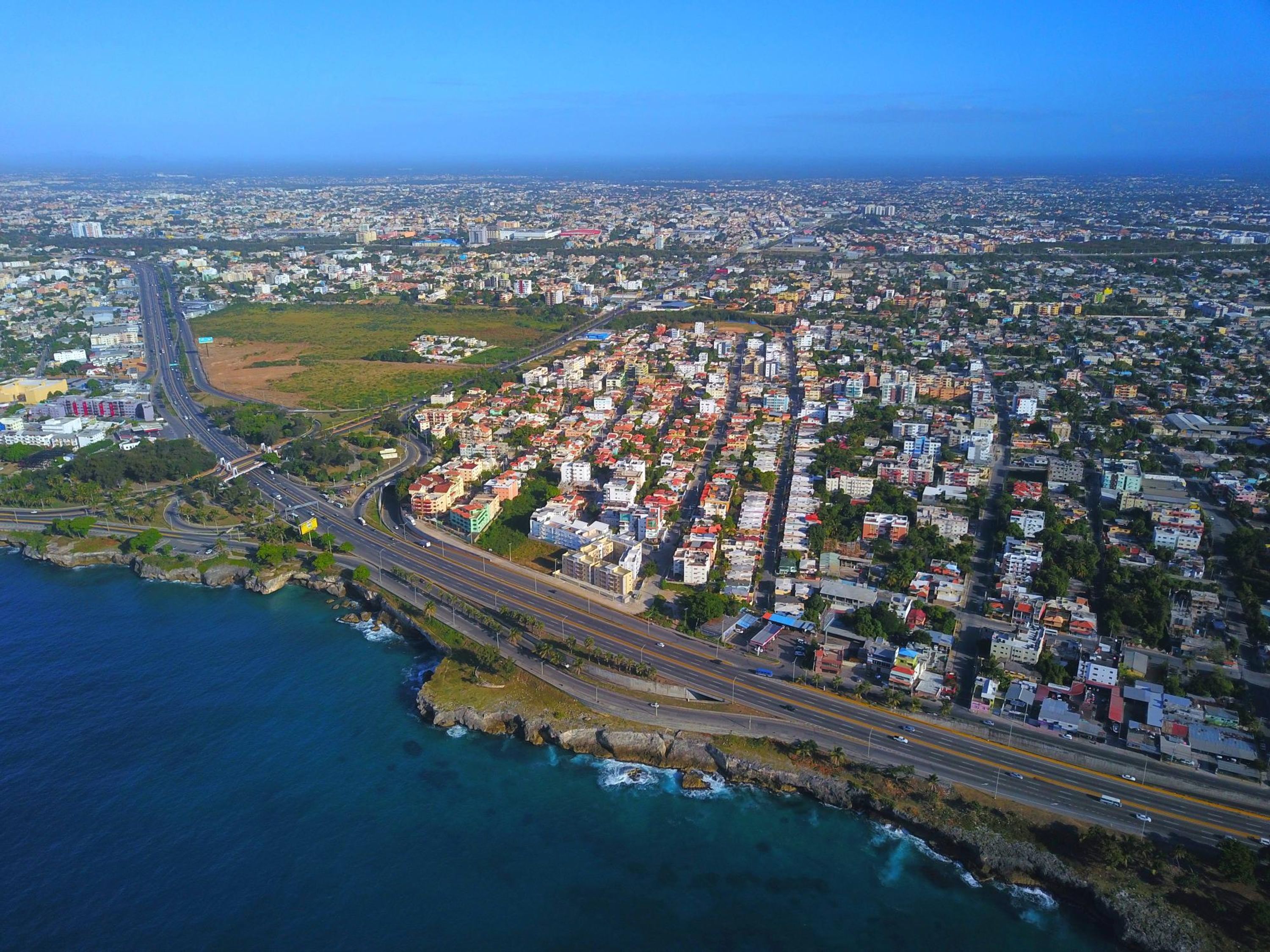 An aerial view of a coastal city with a dense residential area, a major highway, and a coastline.