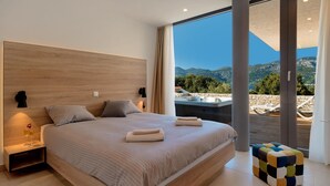 Una camera da letto moderna con un ampio letto, vista sulle montagne e una vasca idromassaggio esterna.