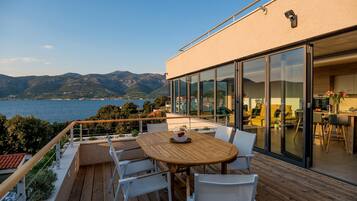 A modern outdoor deck with a wooden table and chairs, overlooking a body of water and mountains.