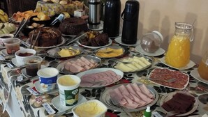 Une table de buffet proposant une variété d’aliments et de boissons, notamment des gâteaux, des viandes, des fromages et une cafetière.