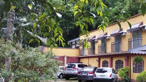 Un bâtiment jaune doté de nombreuses fenêtres et de balcons, entouré de verdure et de voitures garées.