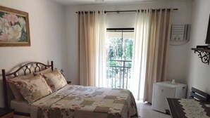 Une chambre à coucher avec un lit, une table de chevet, un radiateur, une fenêtre avec des rideaux et un tableau accroché au mur.