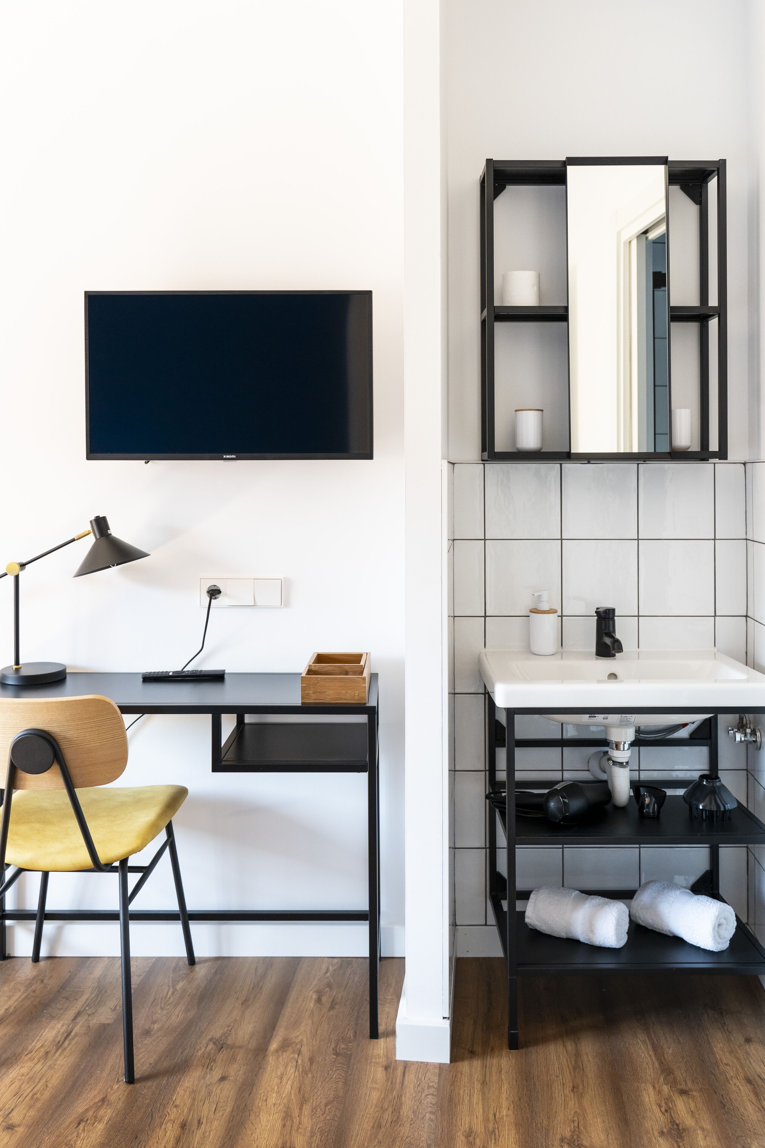 A modern room with a desk, chair, TV, and a bathroom with a sink and mirror.