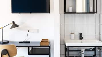A modern room with a desk, chair, TV, and a bathroom with a sink and mirror.