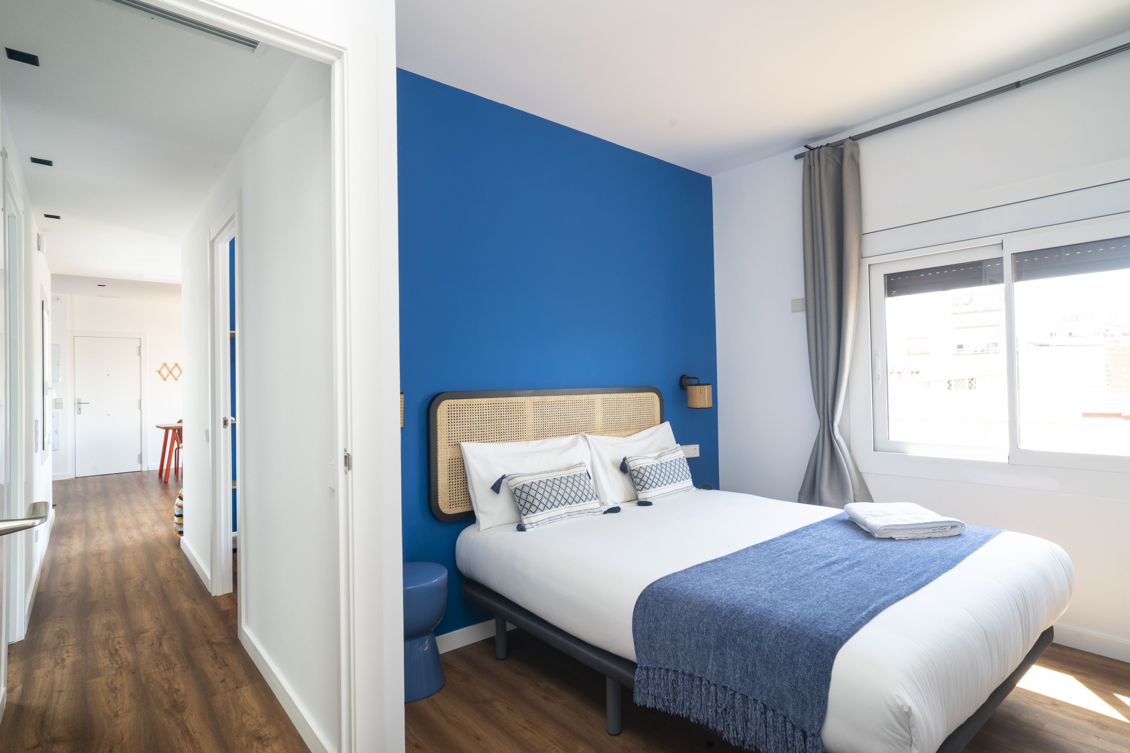 Un dormitorio con una cama, una ventana con cortinas, una mesita de noche y suelo de madera.