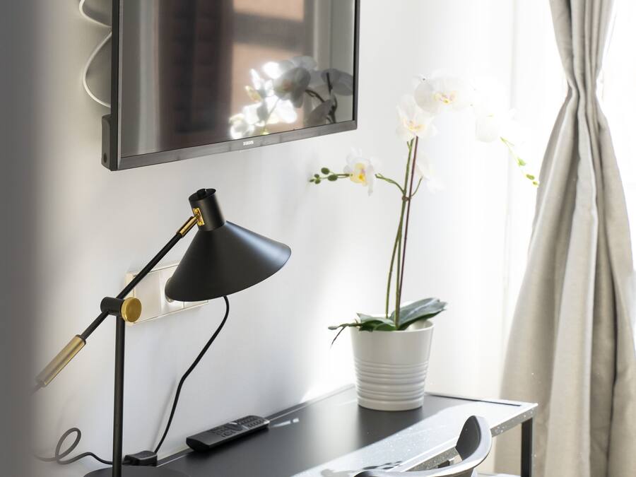 A modern desk with a black desk lamp, a remote control, and a potted orchid.