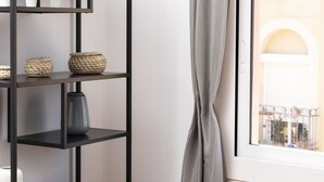 A modern room with a black metal shelving unit, a grey curtain, and a view of a building through a window.
