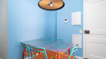 A room with a blue wall, a white door, a table with orange chairs, and a ceiling fan.