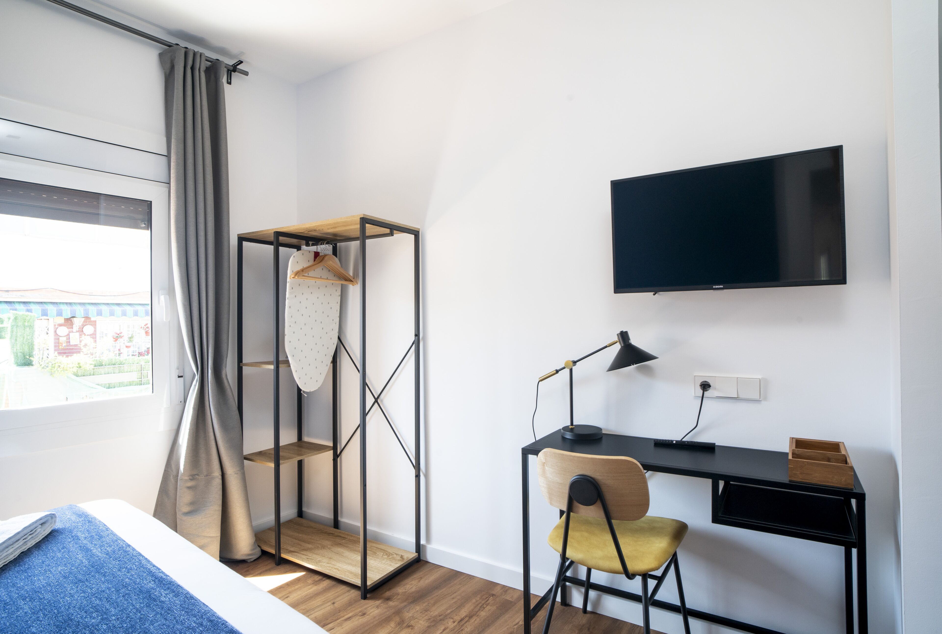 A modern bedroom with a bed, a desk, a chair, a TV, and a wardrobe.