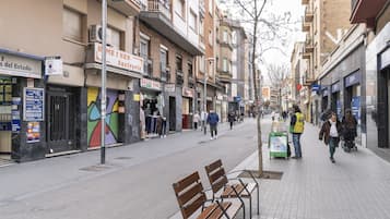 Una calle con bancos, tiendas y gente caminando.