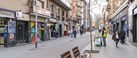Una calle con bancos, tiendas y gente caminando.