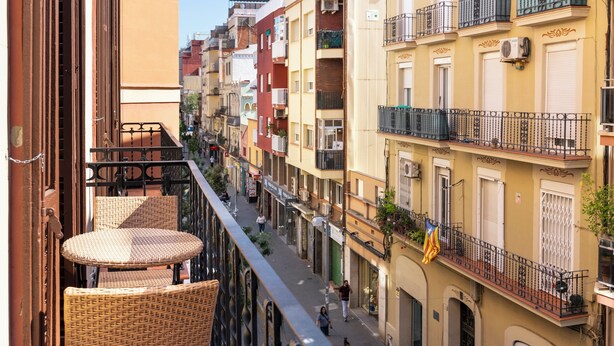 A narrow street lined with multi-story buildings, balconies, and outdoor seating.