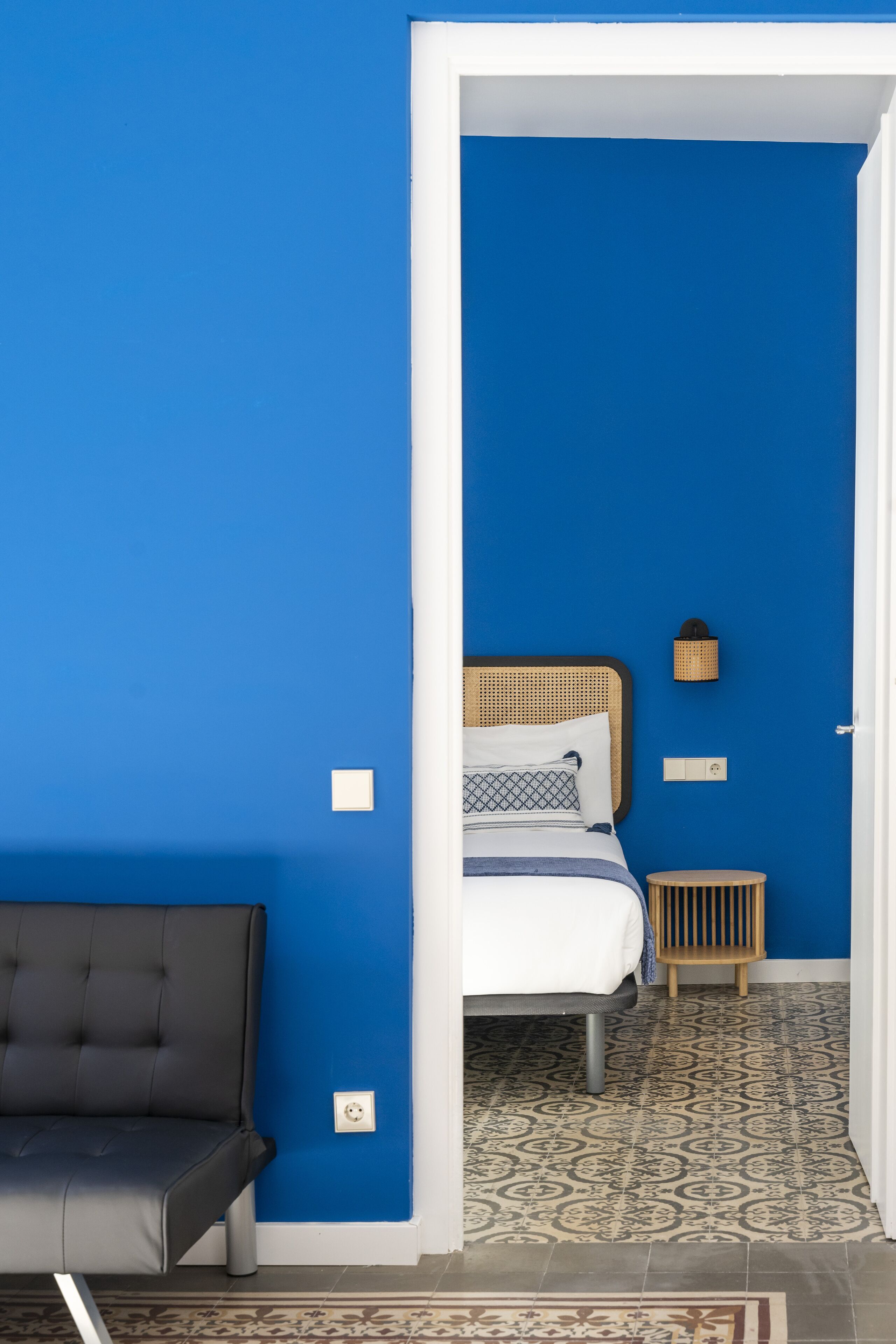 A room with a blue wall, a bed with a wooden headboard, a bedside table, and a small lamp.