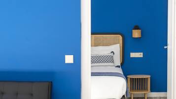A room with a blue wall, a bed with a wooden headboard, a bedside table, and a small lamp.