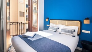 A hotel room with a large bed, a balcony with a view of other buildings, and a blue accent wall.