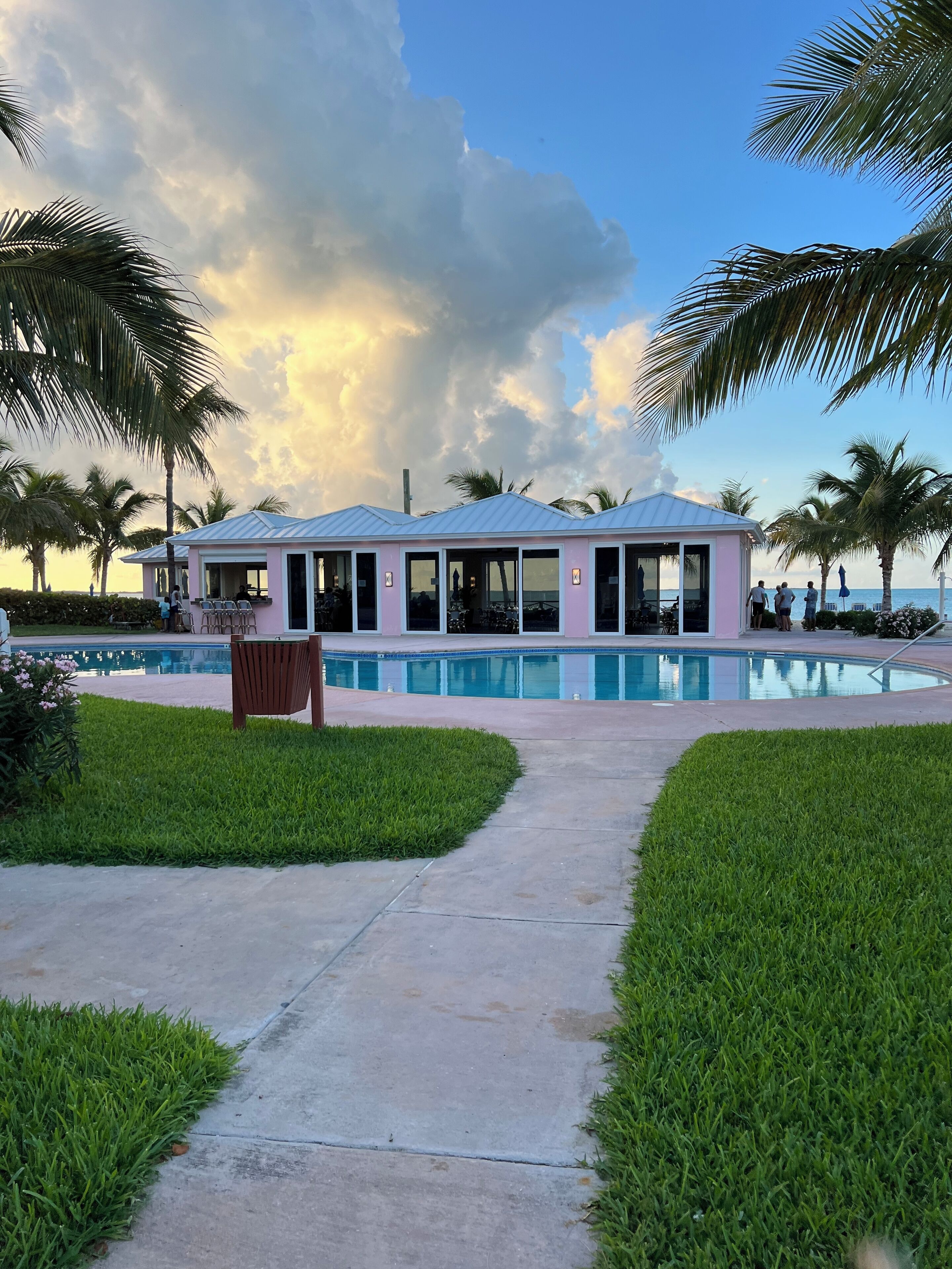 A pink building with a pool, surrounded by palm trees and a clear sky.