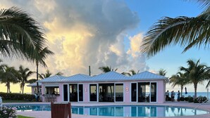 A pink building with a pool, surrounded by palm trees and a clear sky.